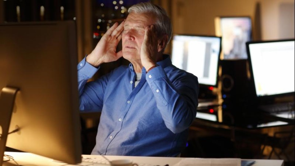 Man met handen aan het hoofd en ogen dicht voor beeldscherm