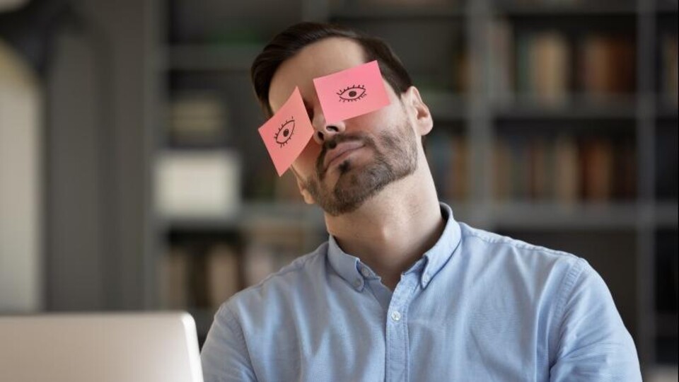 Man slaapt achter pc met stickers van open ogen op zijn ogen