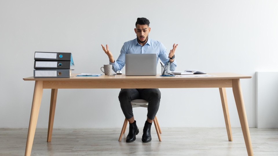 Man kijkt vertwijfeld naar laptop met documenten om zich heen op tafel