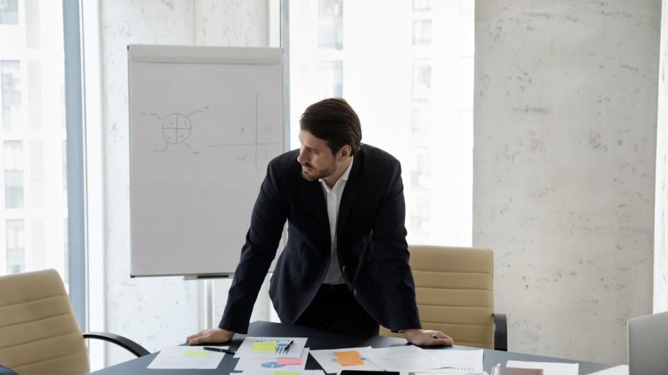 Man aan bestuurstafel vol schema's en plaknotes, staart uit het raam
