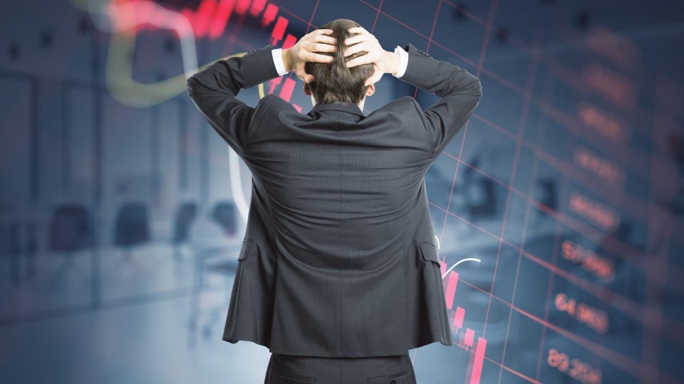 Man staat met handen in het haar te kijken naar scherm met dalende grafiek