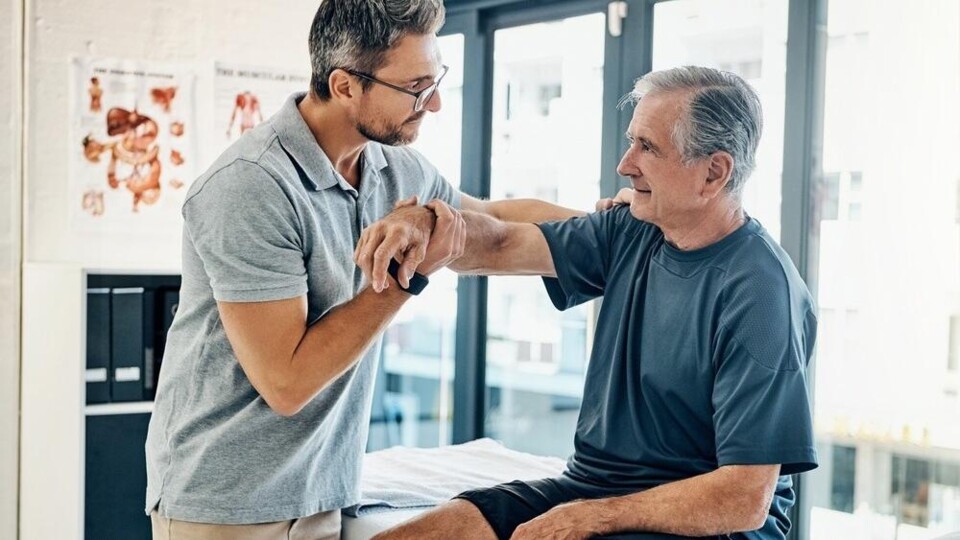 Een fysiotherapeut helpt iemand om de arm omhoog te doen