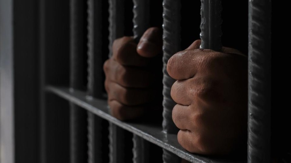 Twee handen houden tralies vast