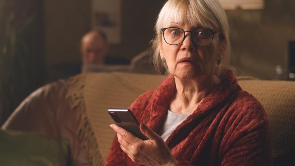 Oudere in kamerjas kijkt onthutst op van smartphone