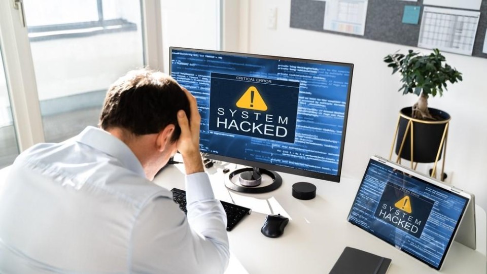 Man achter een computer, met daarop een melding dat hij gehackt is
