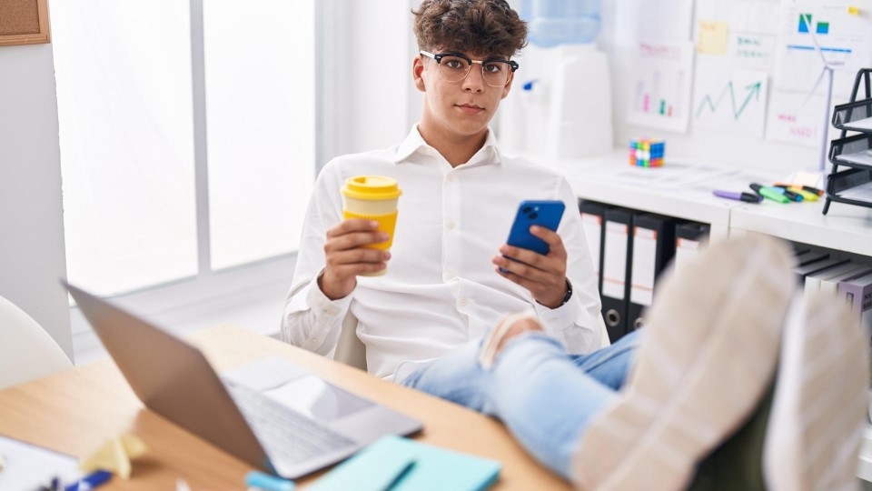 Teenager zit met benen op bureau te kijken naar zijn smartphone
