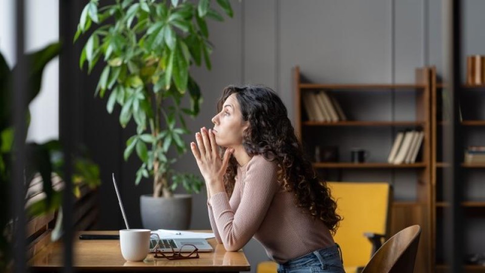 Vrouw staart in gedachten over haar laptop naar buiten 