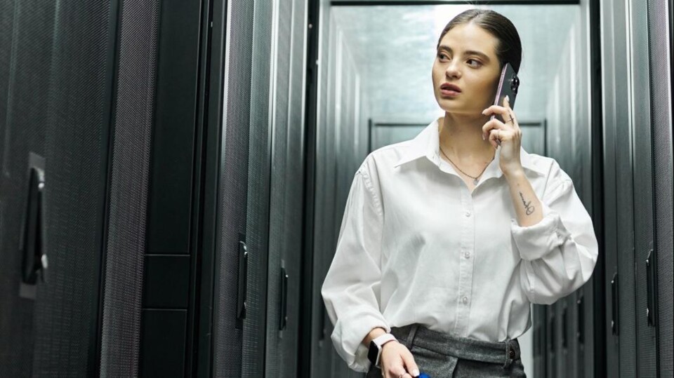 Vrouw met smartphone in de hand kijkt wantrouwend naar serverkast in een datacentrum