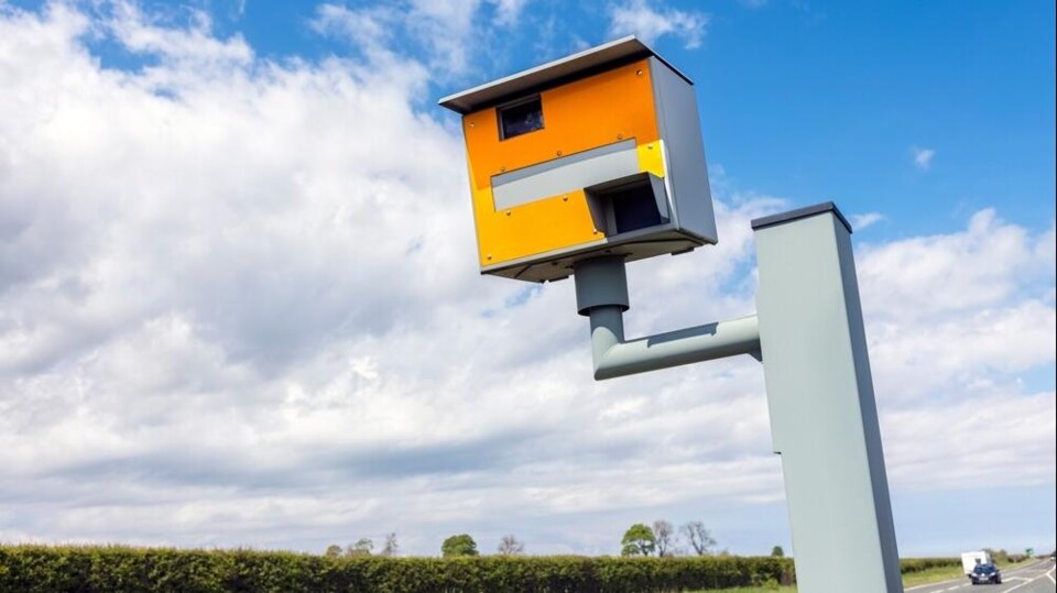 Gele snelheidscontrolecamera langs Nederlandse snelweg met blauwe hemel