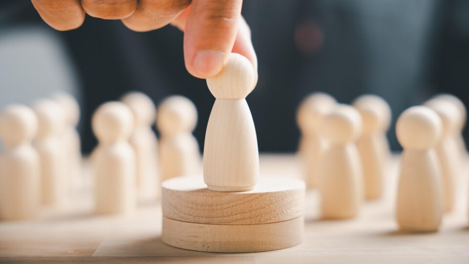 Hand plaatsen houten figuur op een platform, omringd door andere figuren