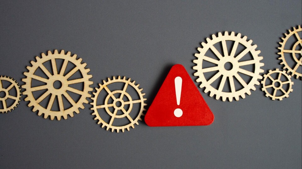 Rood waarschuwingsbord tussen houten tandwielen die industriële risico's en mechanisch systeemfalen vertegenwoordigen