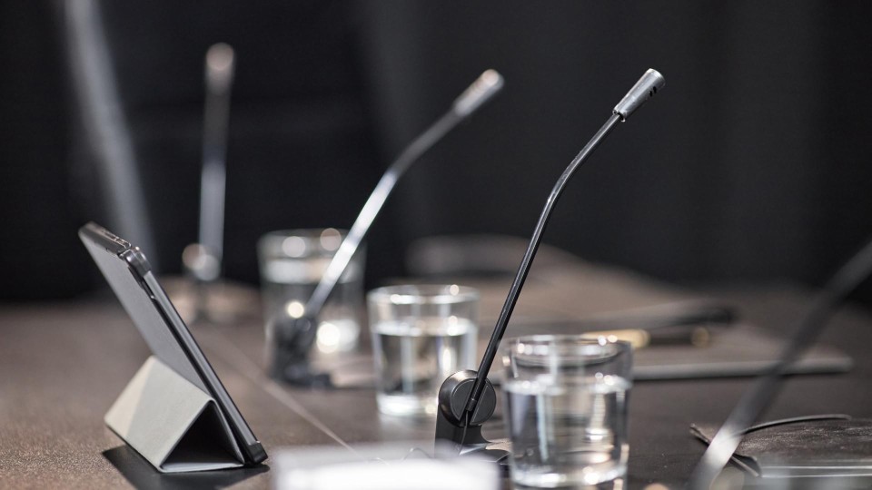Close-up van microfoons, een tablet en volle waterglazen op een lege vergadertafel