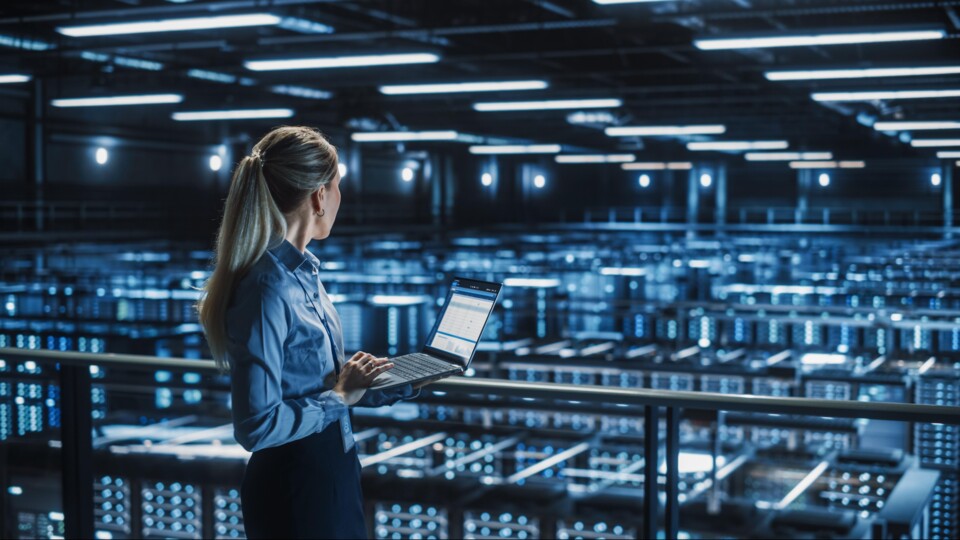 Vrouw staat met laptop in groot datacenter