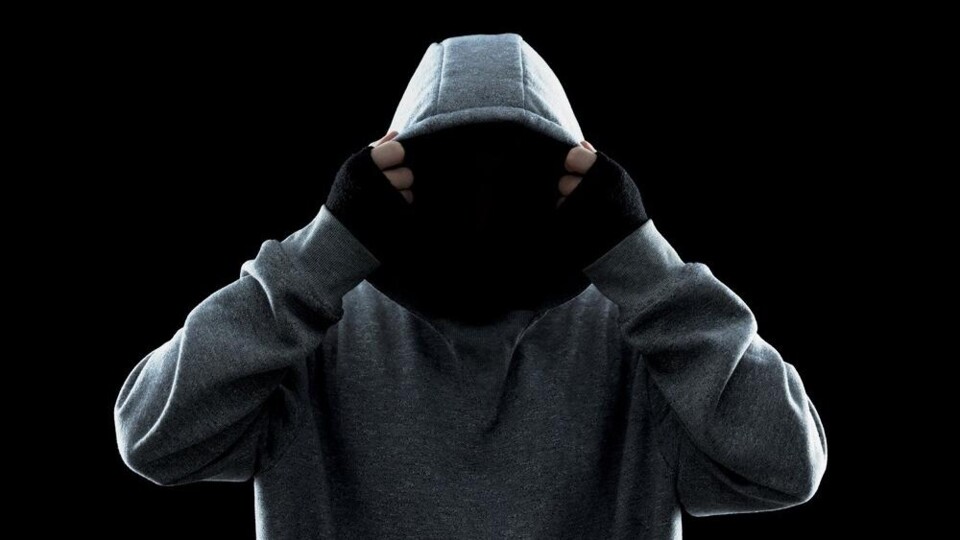 Persoon in grijze hoodie trekt capuchon over het hoofd met zwarte handschoenen, zwarte achtergrond