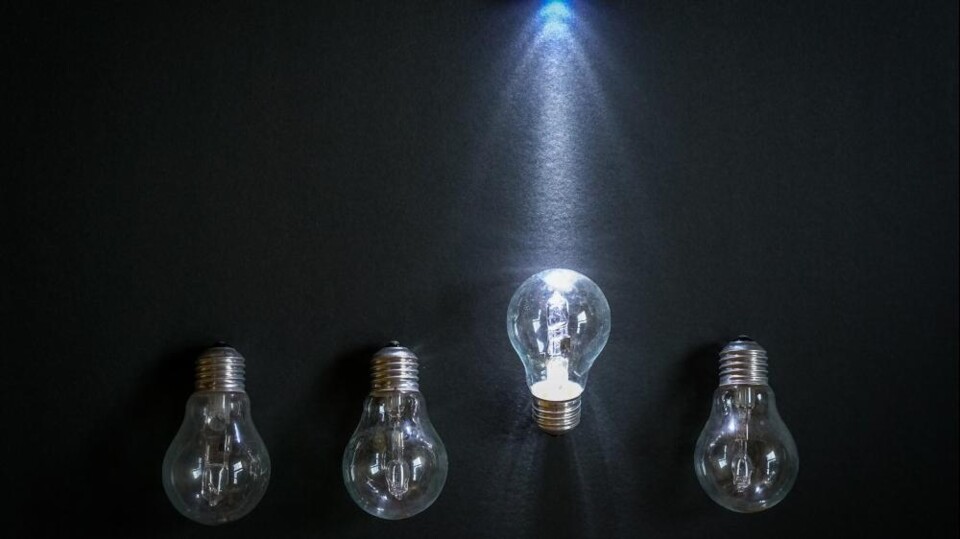 Vier gloeilampen op een rij, waarvan één in het midden brandt onder een blauwe lichtstraal.