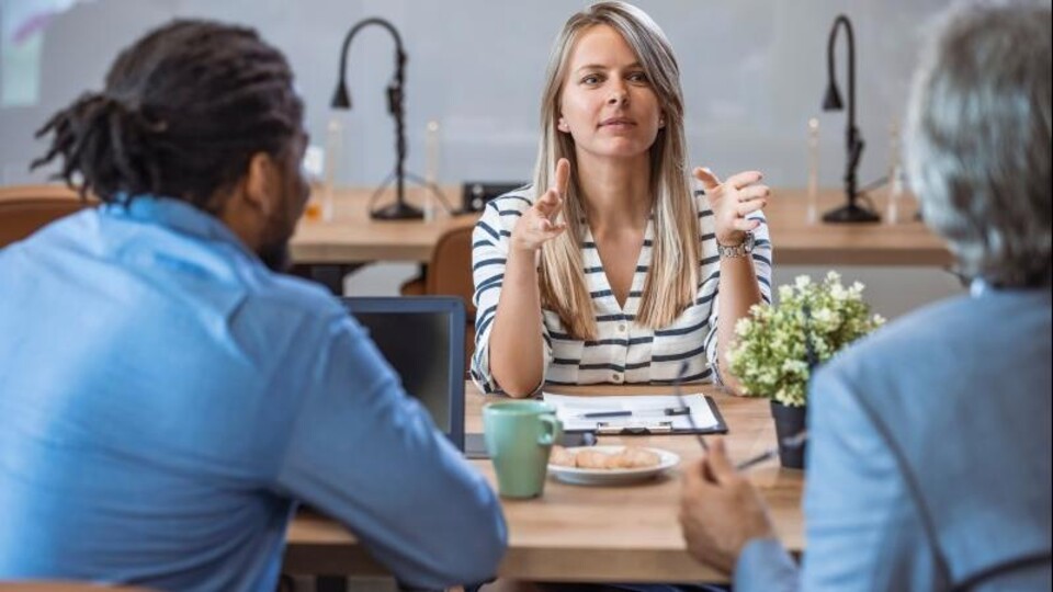 Een vrouwelijke manager zit aan tafel tegenover twee mannen. Het is een zakelijk gesprek.