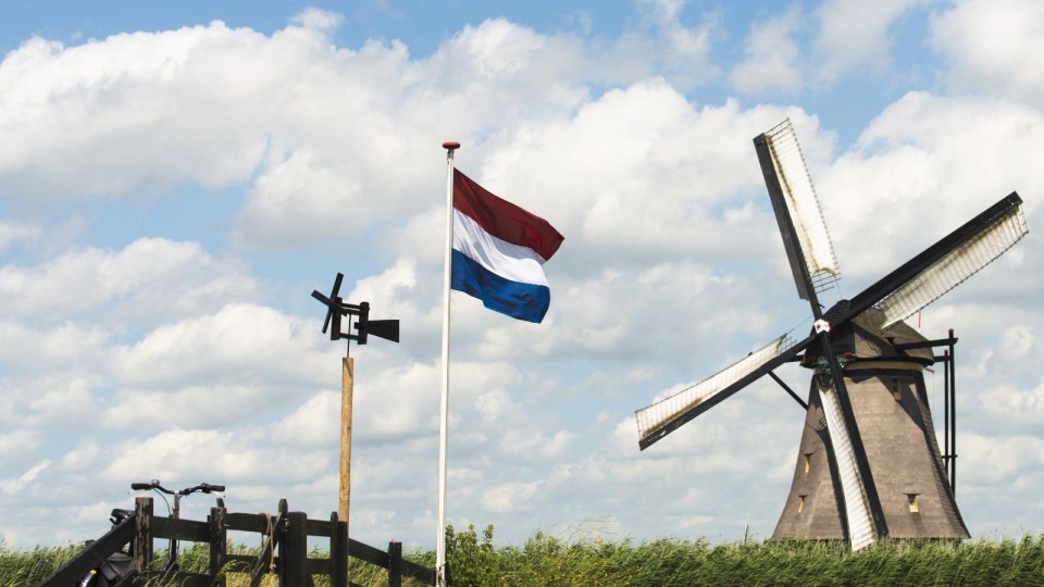 Een molen, een Nederlandse vlag en wolken