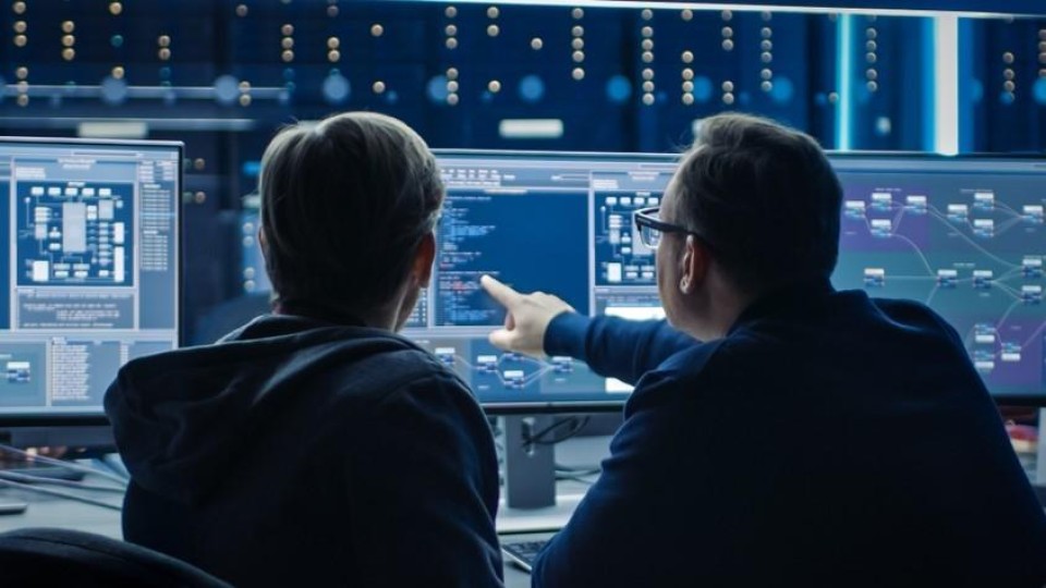 Twee software-ontwikkelaars in gesprek achter een computer met code.