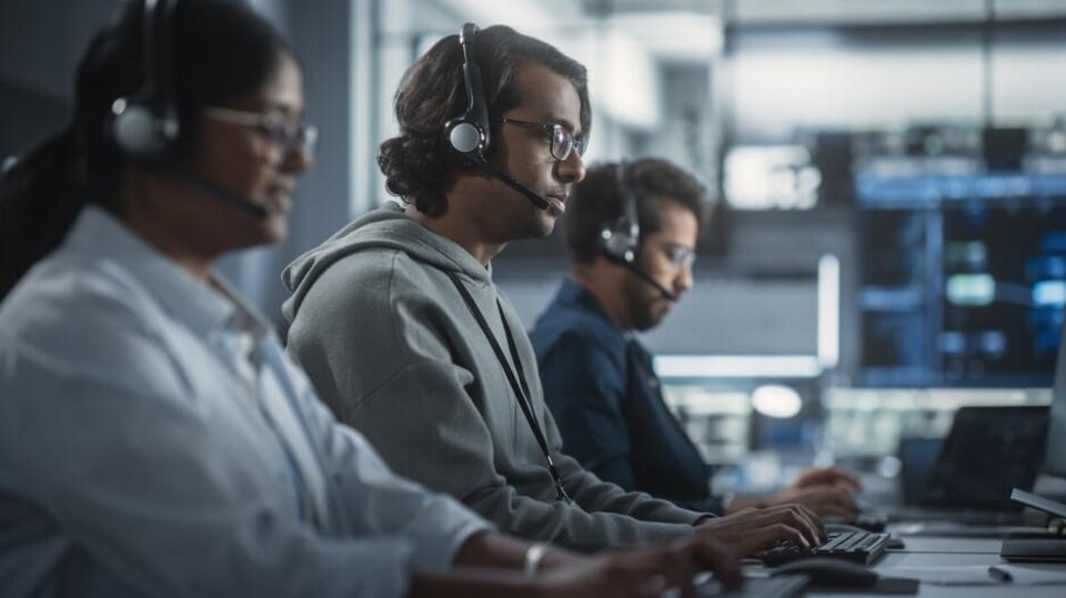 Techsupportmedewerkers, drie, aan het werk achter hun computer, met headsets op.