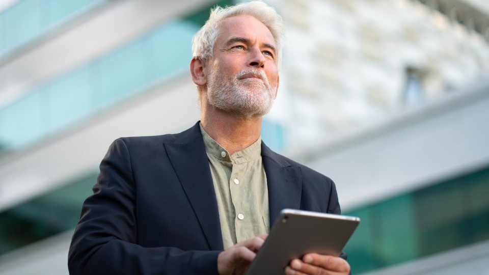 Man kijkt zelfverzekerd weg terwijl zijn hand op een tablet rust