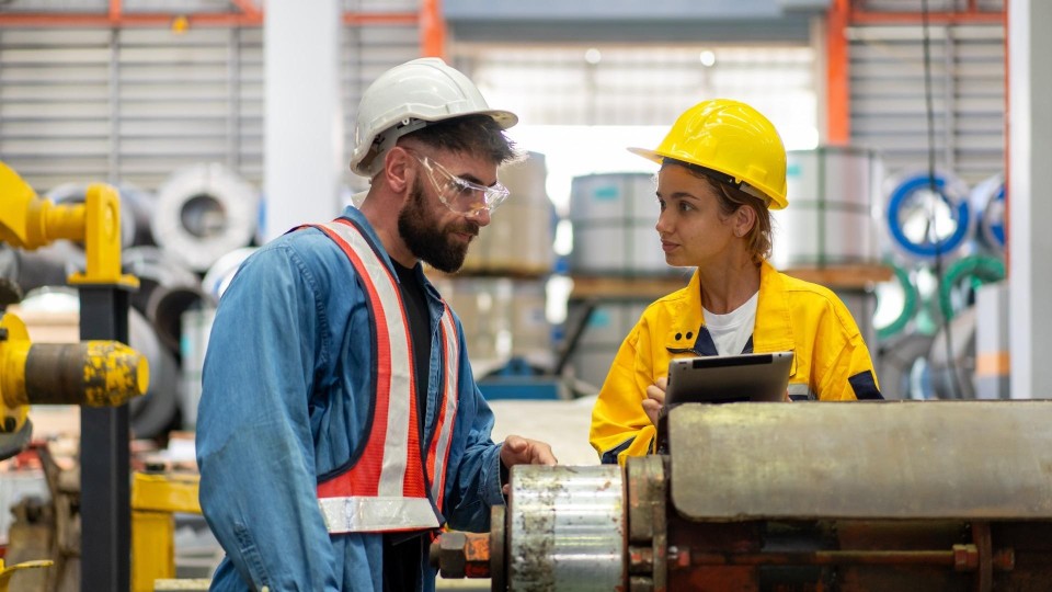 Twee mensen staan gebogen over een tablet in een fabrieksomgeving
