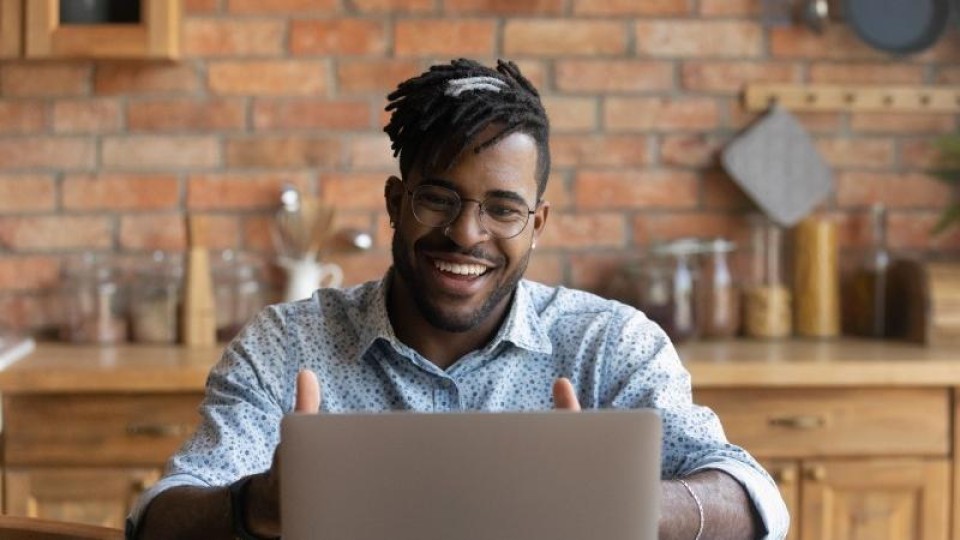 Blije man achter laptop in de keuken steekt duimen op