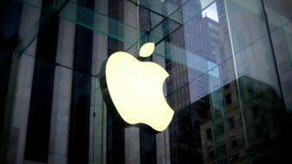 Verlicht Apple-logo op glazen gevel met reflectie van hoge kantoorgebouwen in de achtergrond